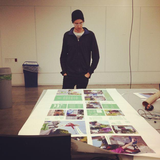 There is a person with glasses looking at a poster on a table. The poster has photos and green squares of text.