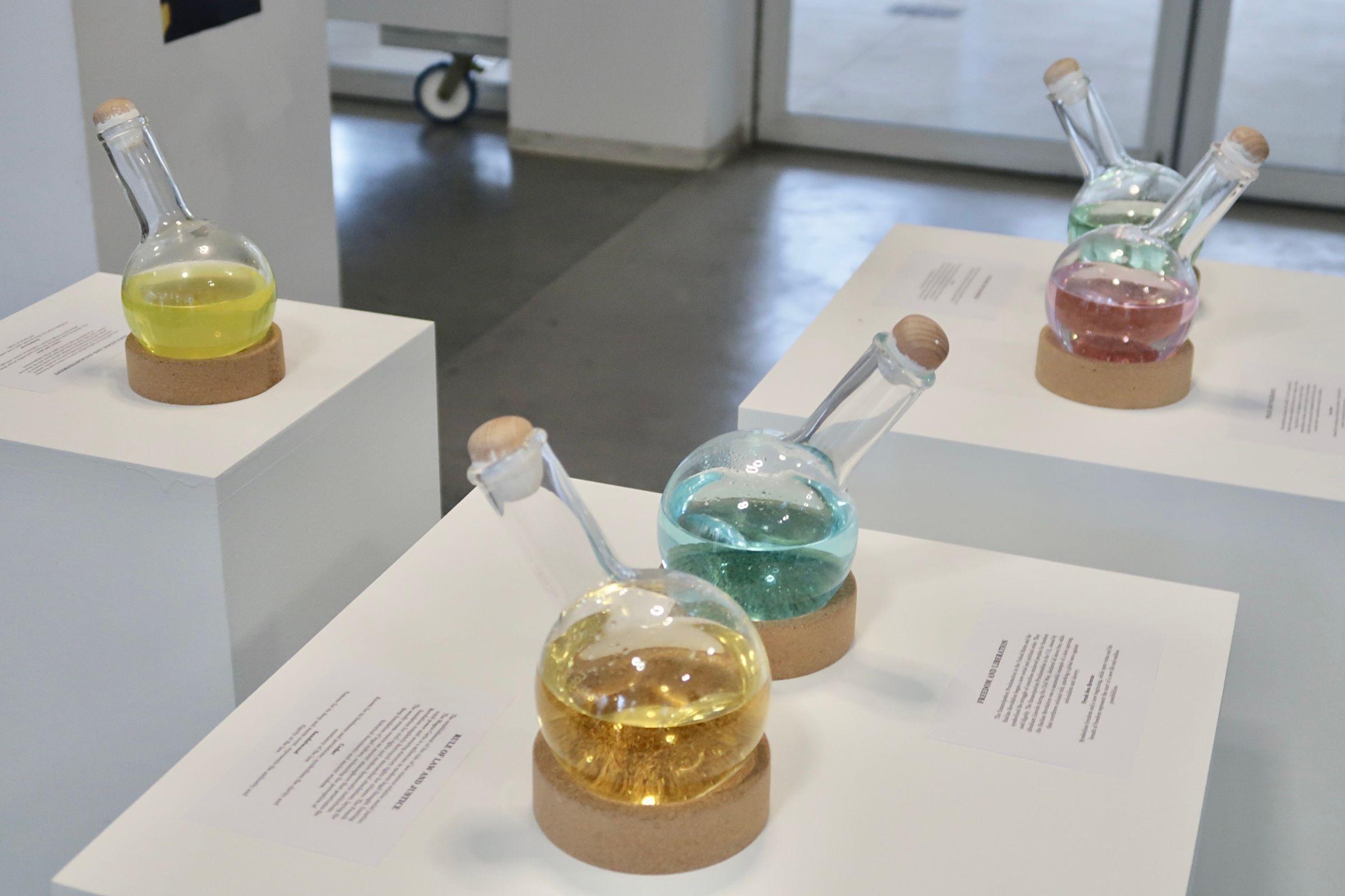 Three tables with vials of colored liquid. The spouts face out toward the audience, inviting them to lean in and smell.