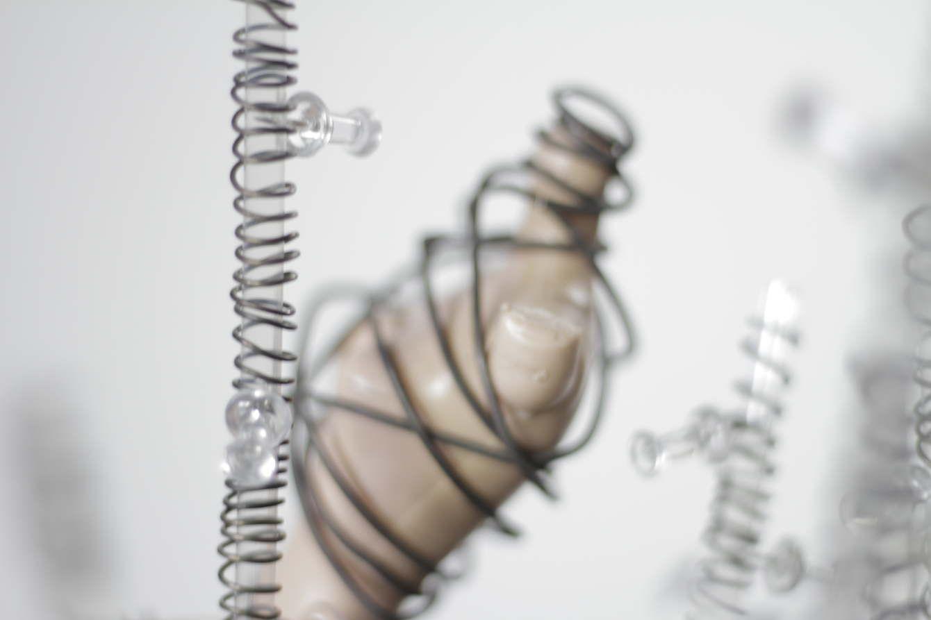 There is a clear rod with wire wrapped around it and push pins stuck inside. In the background, there are more clear rods with wire and pushpins and also a doll body without arms wrapped with wire.