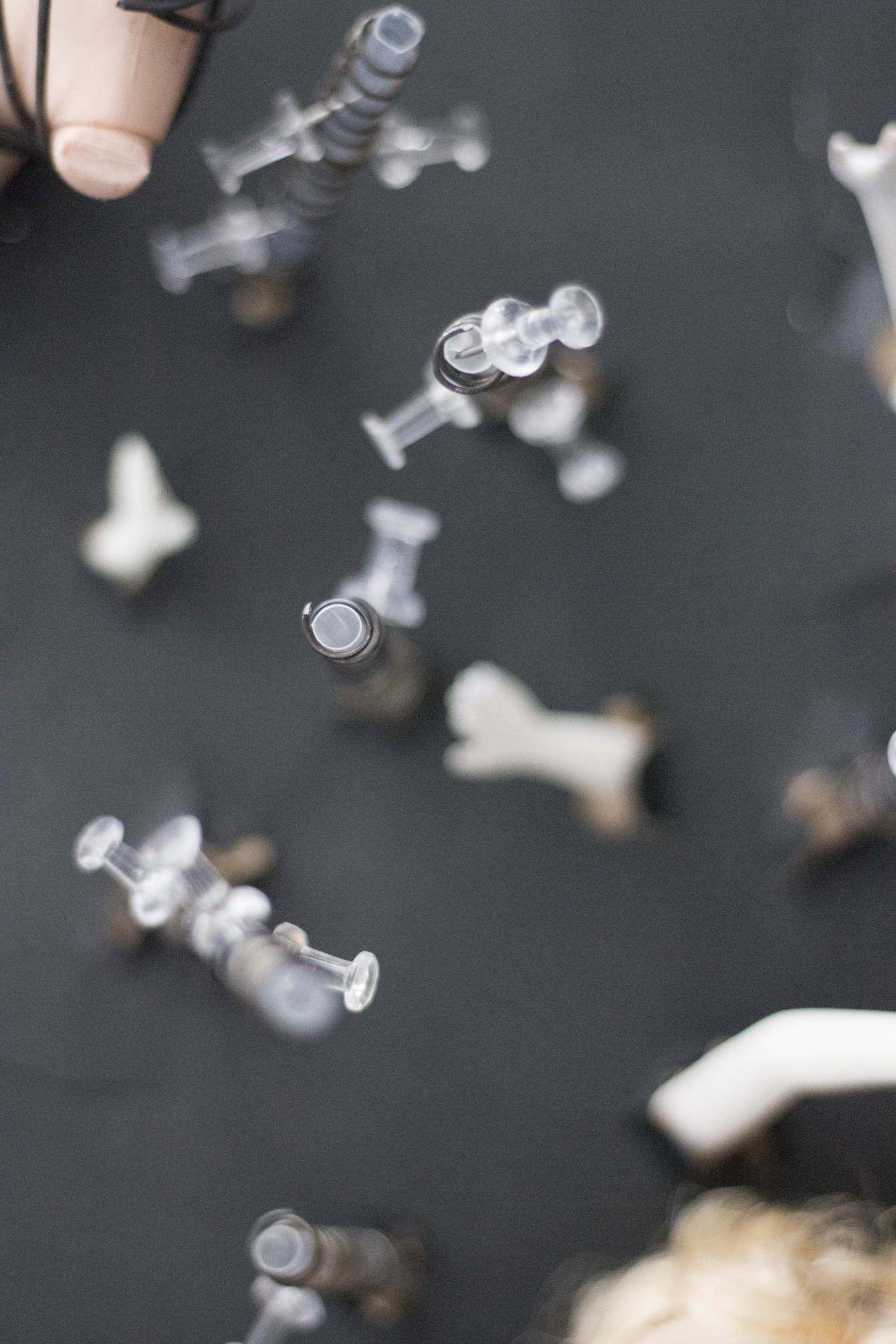 There are various pushpins arranged on the photo. The rest of the photo is blurry. There seem to be pieces of dolls on the table where the pushpins are located.