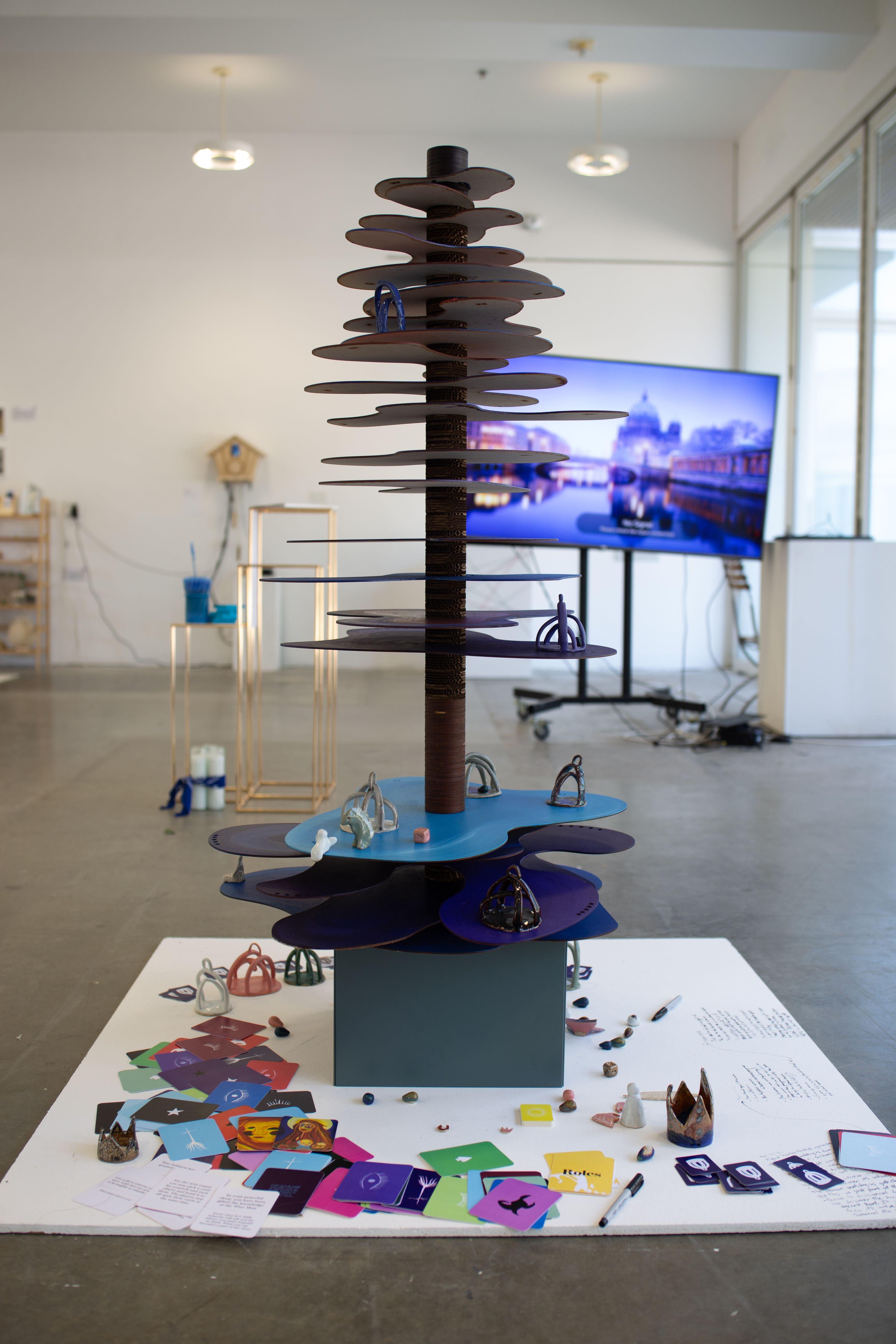 A tower with many layers of irregular, oval shaped platforms. Game cards and crown-shaped game pieces are scattered around the base of the tower.